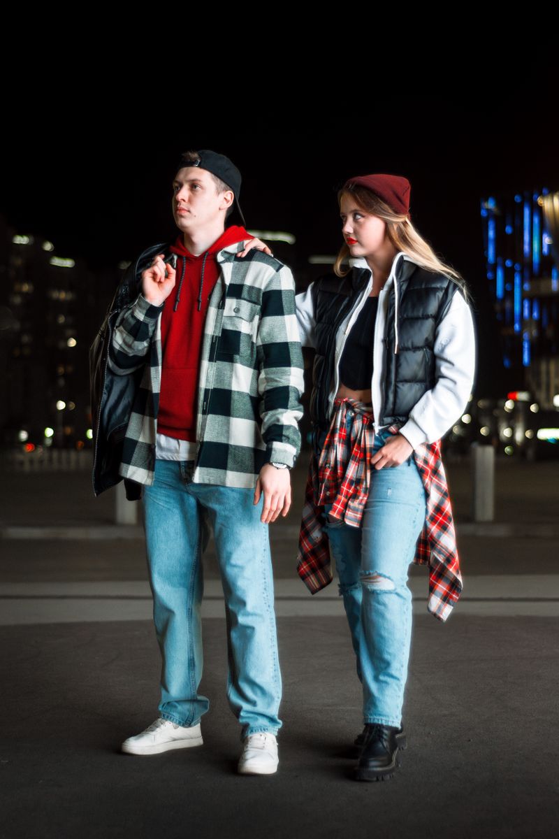 A stylish young couple in urban streetwear posing confidently on a city street at night.